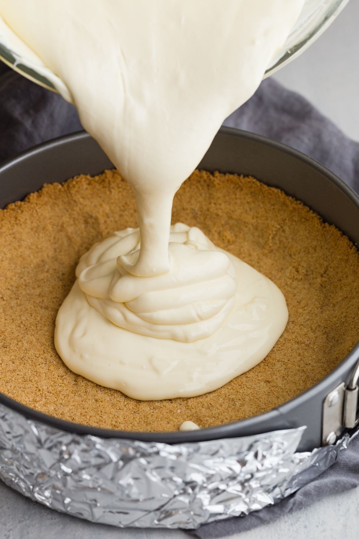 cheesecake filling being poured in graham cracker crust