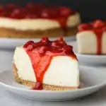 Side view of slice of strawberry cheesecake on white plate.