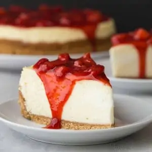 Side view of slice of strawberry cheesecake on white plate.