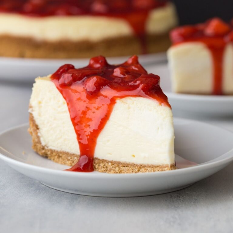 Side view of slice of strawberry cheesecake on white plate.