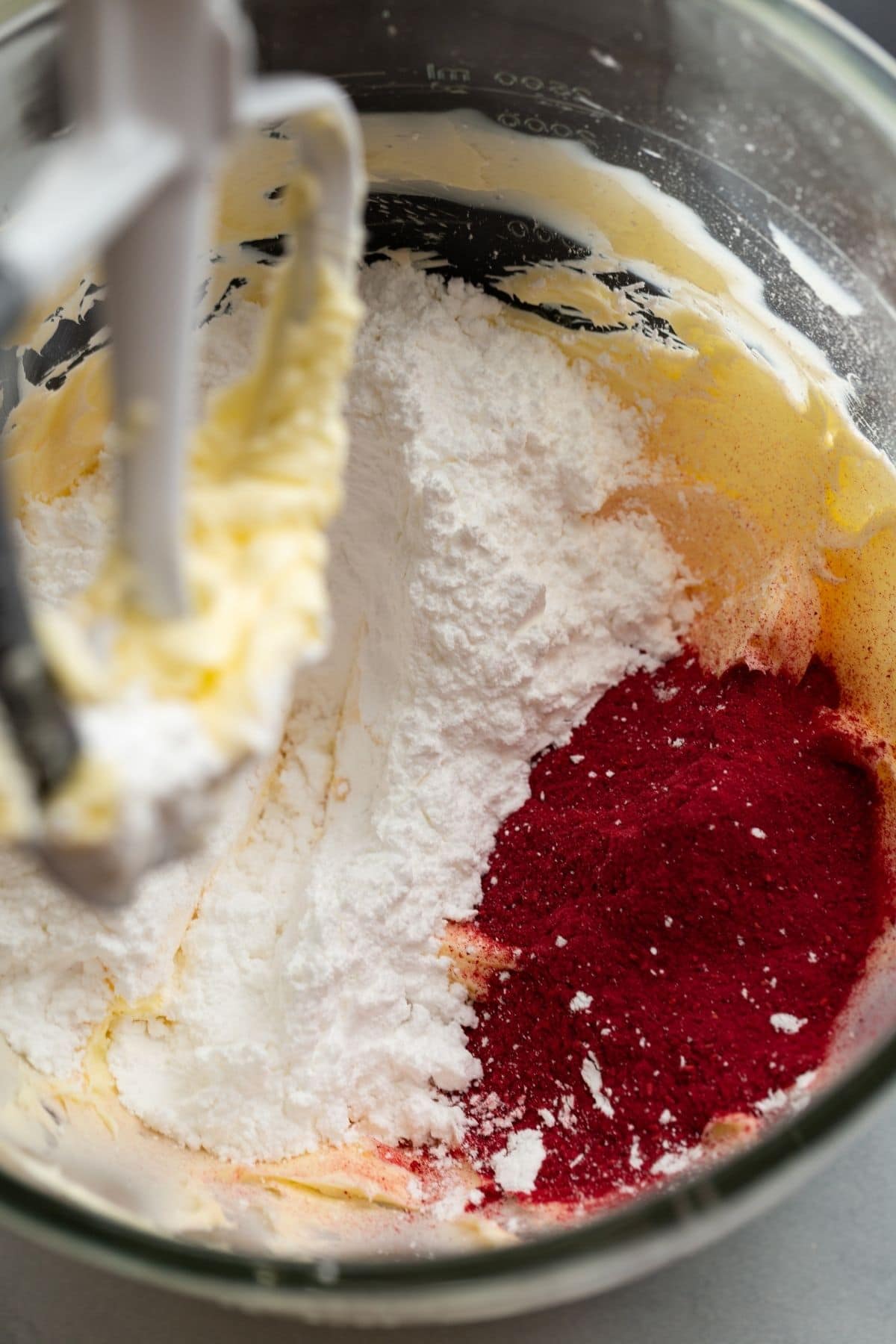 Creamed butter with powdered sugar and raspberry powder in glass bowl.