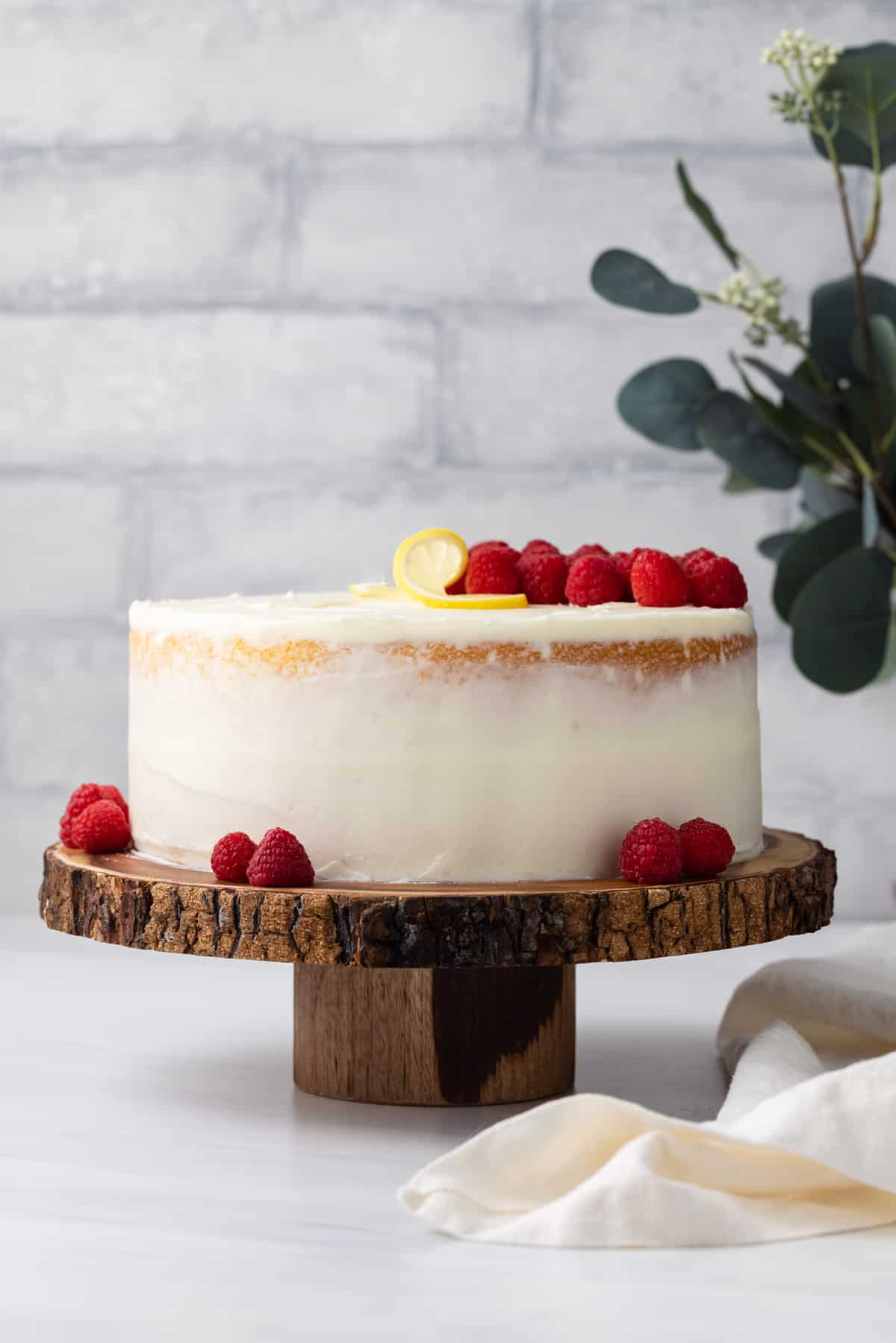 Lemon raspberry cake on a serving stand with fresh raspberries