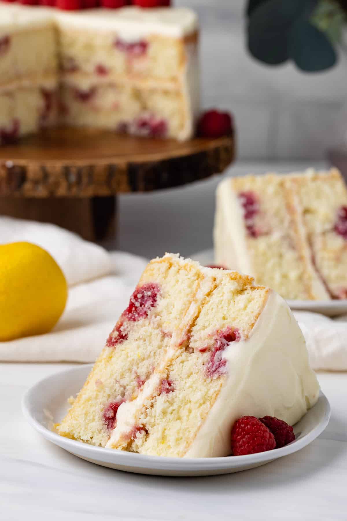 A slice of lemon raspberry cake on a plate in front of the lemon raspberry cake