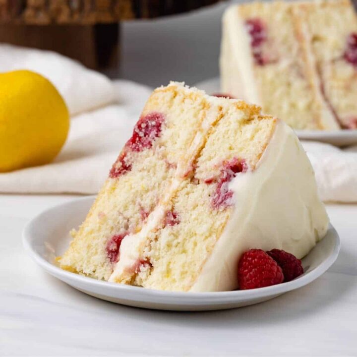 A slice of lemon raspberry cake on a plate in front of the lemon raspberry cake
