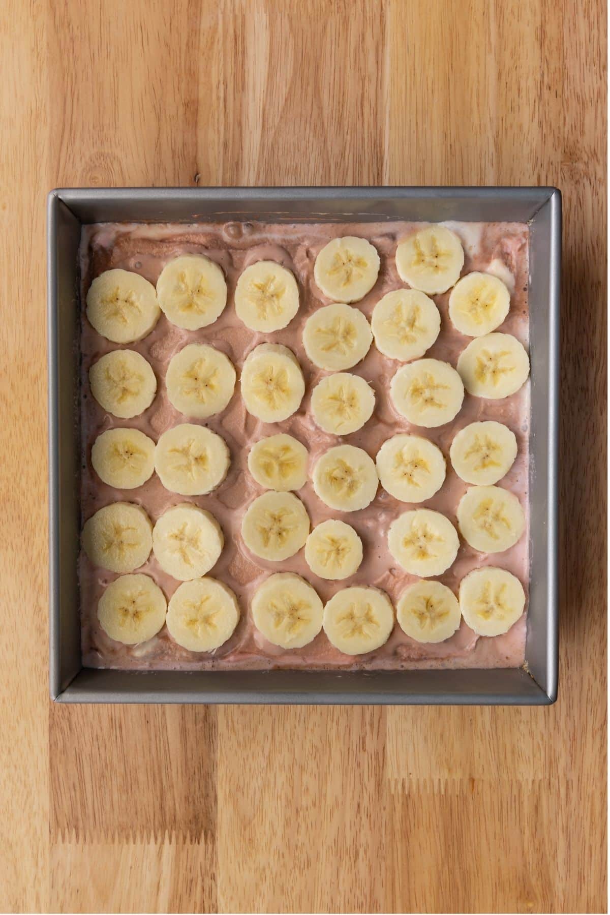 Banana slices over ice cream in square pan.