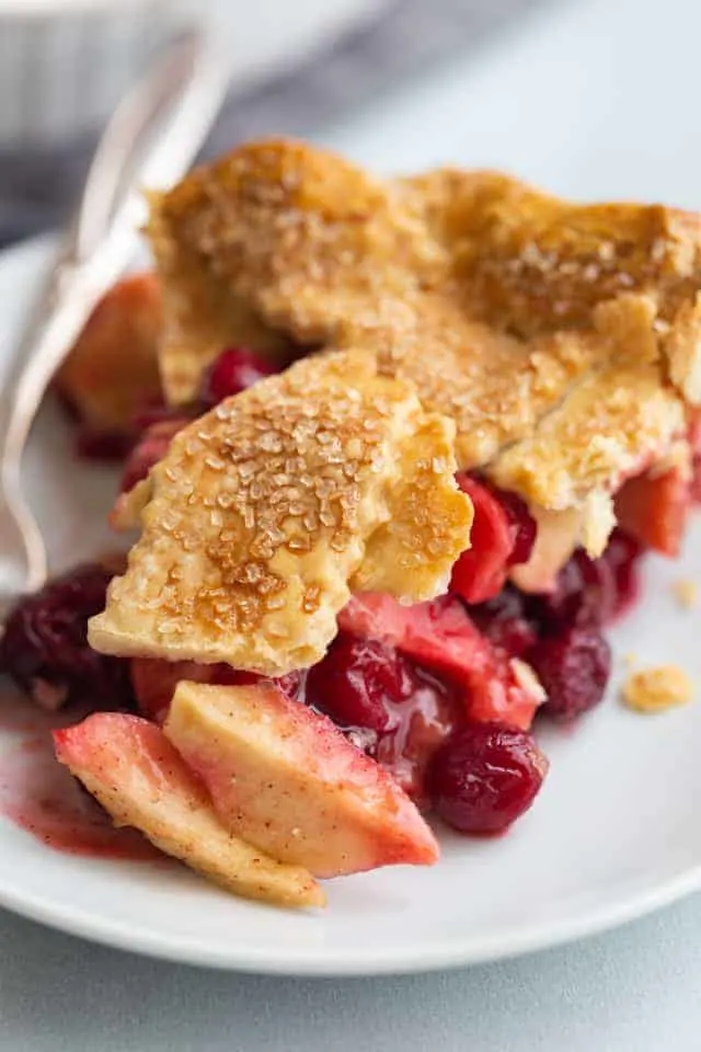 close up of a slice of apple cranberry pie on a white plate