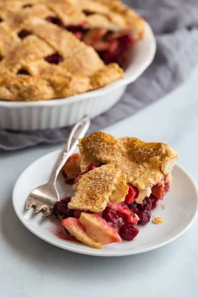 side view of a slice of apple cranberry pie on a white plate