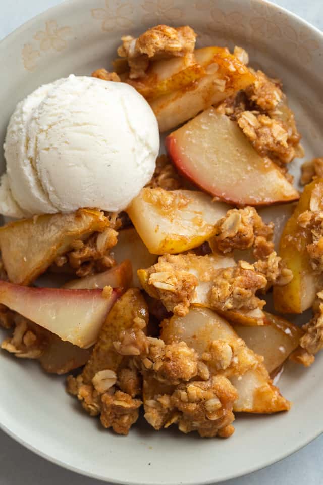 close up view of pear crisp in a bowl with a scoop of ice cream