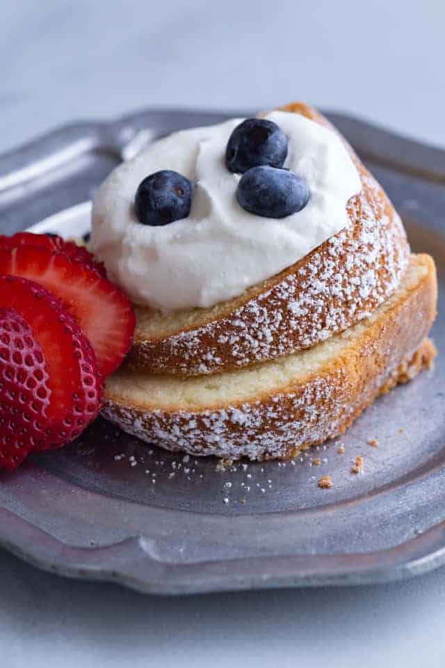 two slices of sour cream pound cake topped with whipped cream, blueberries, and strawberries