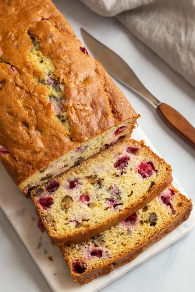 angled view of cranberry walnut bread sliced on a marble cutting board