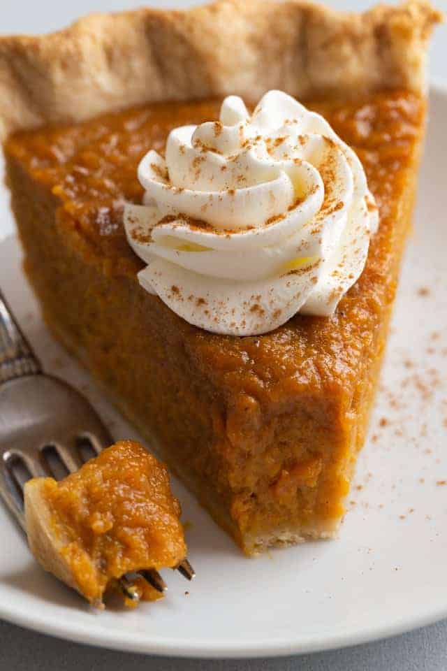 close up view of a slice of sweet potato pie with a fork taking a bite out