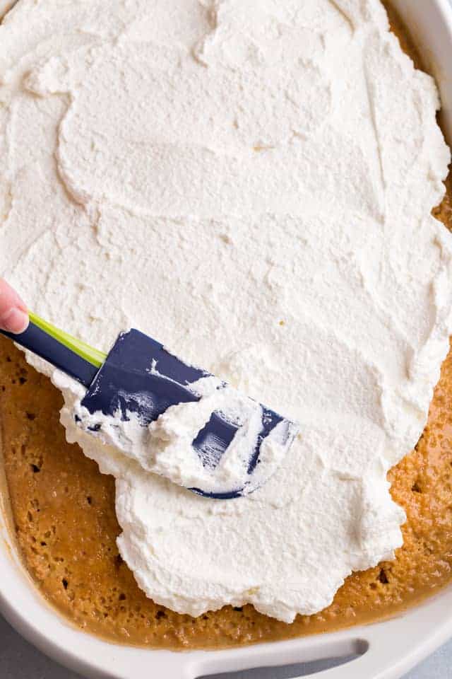 whipped cream being spread over tres leches cake