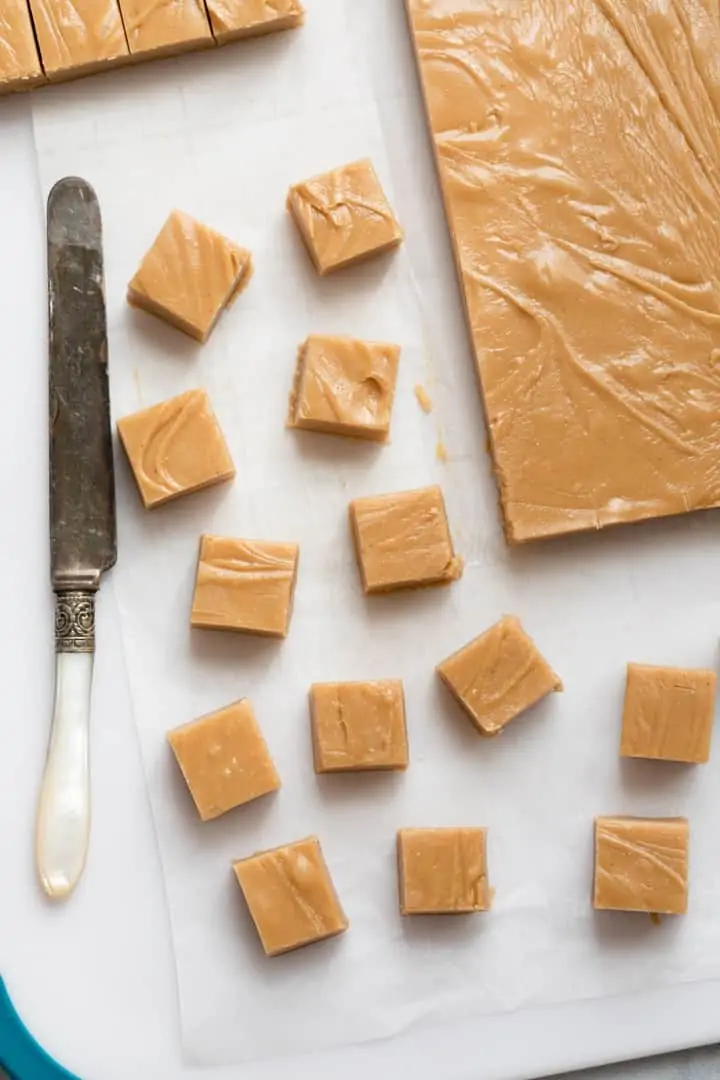 creamy peanut butter fudge being sliced into squares on white cutting board