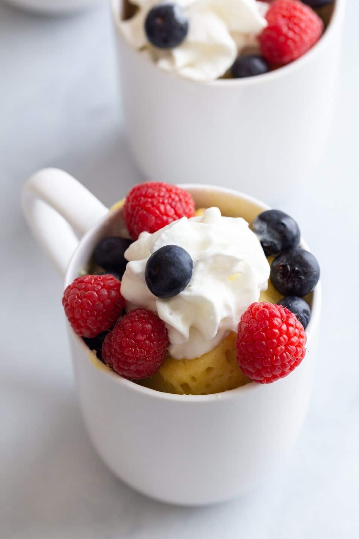 Angled view of vanilla mug cake recipe with whipped cream and fresh berries.