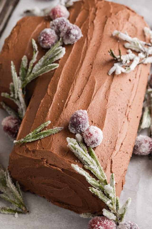angled view of yule log cake with sugared rosemary and cranberries