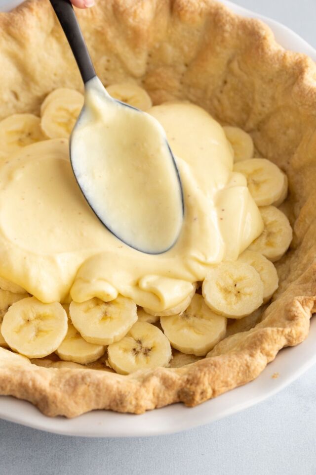 Vanilla pudding being spread over bananas in a baked pie shell.