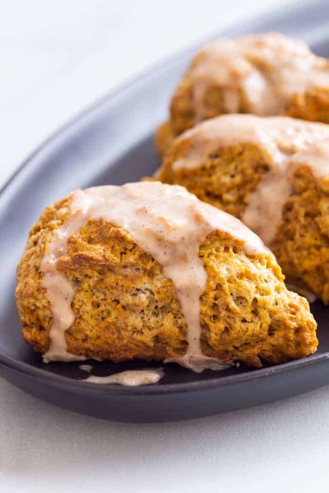 side view of pumpkin scones topped with spiced glaze on a dark blue plate