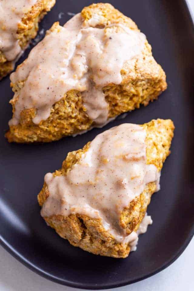 overhead view of pumpkin scones topped with spiced glaze on a dark blue plate