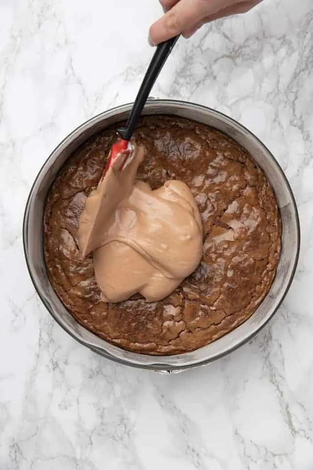 Nutella mousse being spread over a Nutella brownie in a round pan