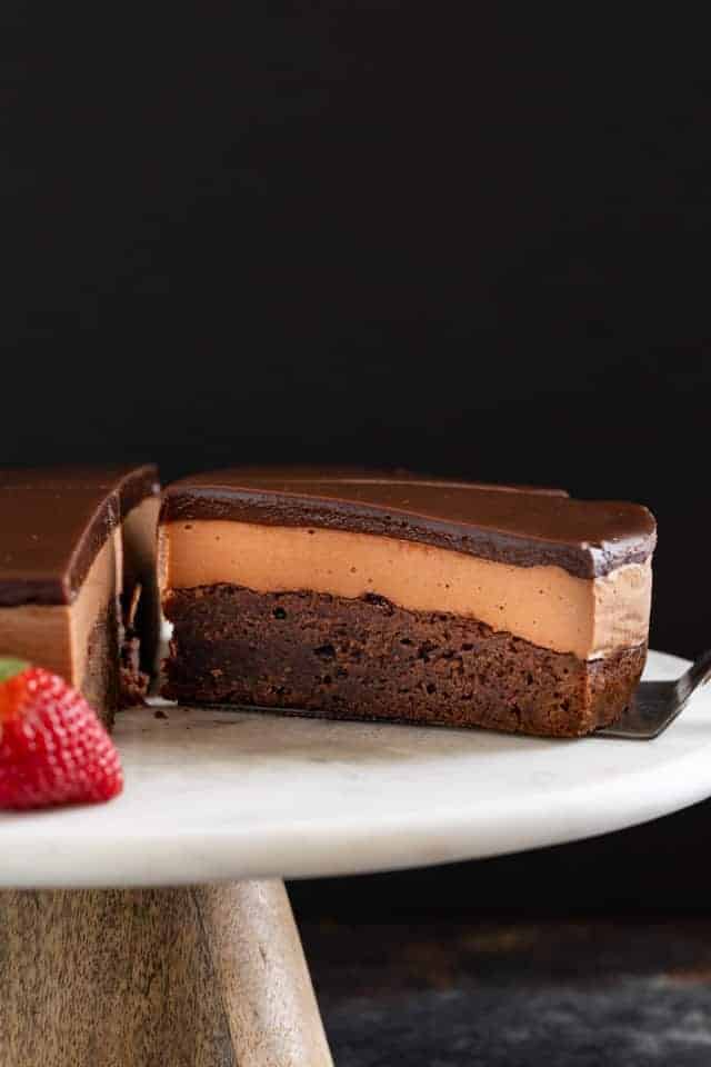 Triple Nutella mousse cake on a cake plate with a slice being taken out.