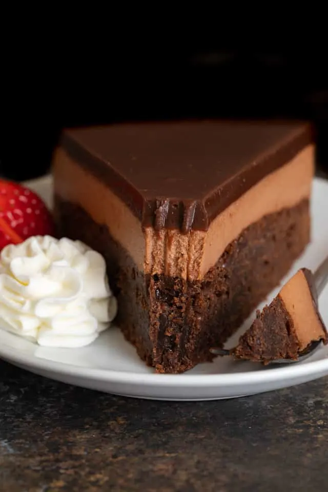 Slice of triple Nutella mousse cake on a white plate with a fork taking out a bite.