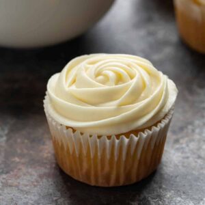 Side view of cream cheese frosting swirled over yellow cupcakes