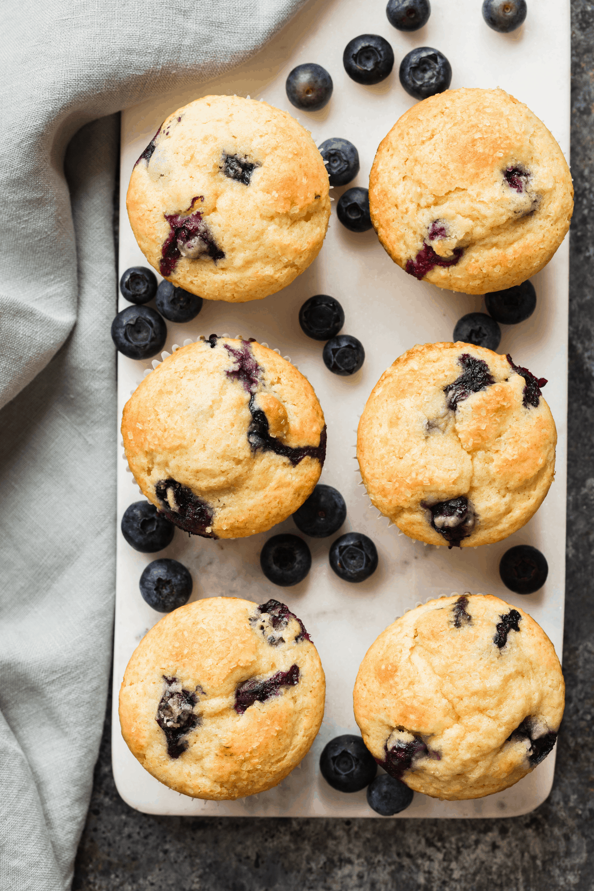 overhead view of blueberry muffins on a marble board with blueberries scattered around
