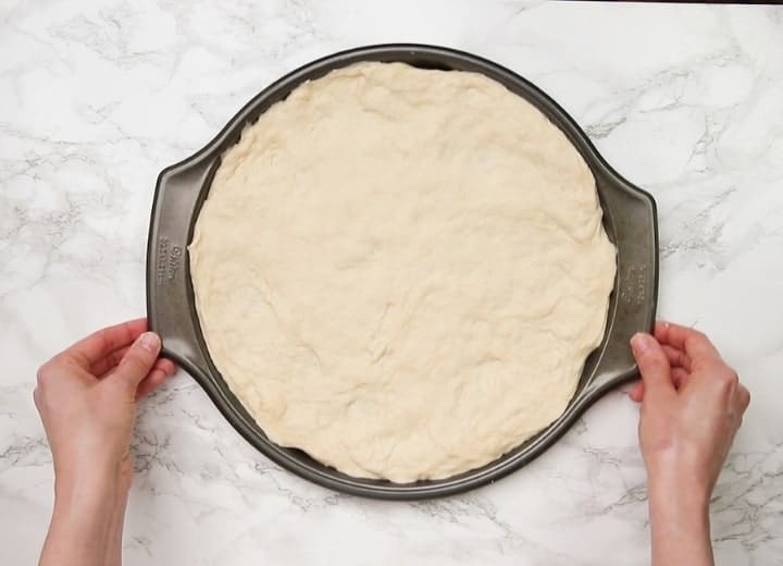 unbaked pizza dough on a pizza pan