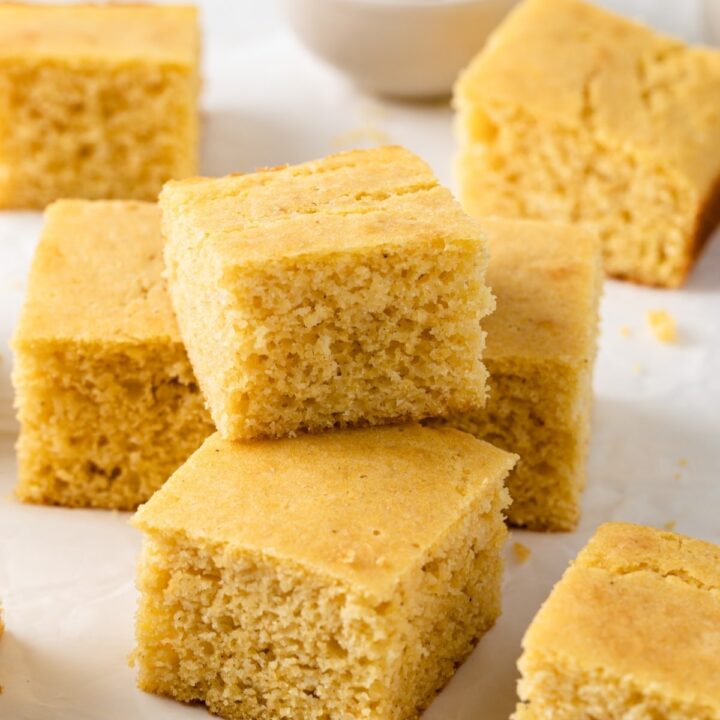 southern cornbread squares stacked on a white background with bowl of butter behind