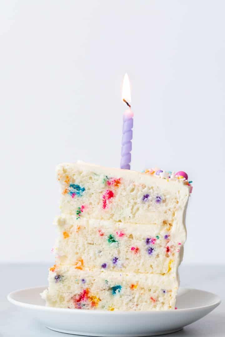 slice of funfetti cake on a white plate with a purple candle on top