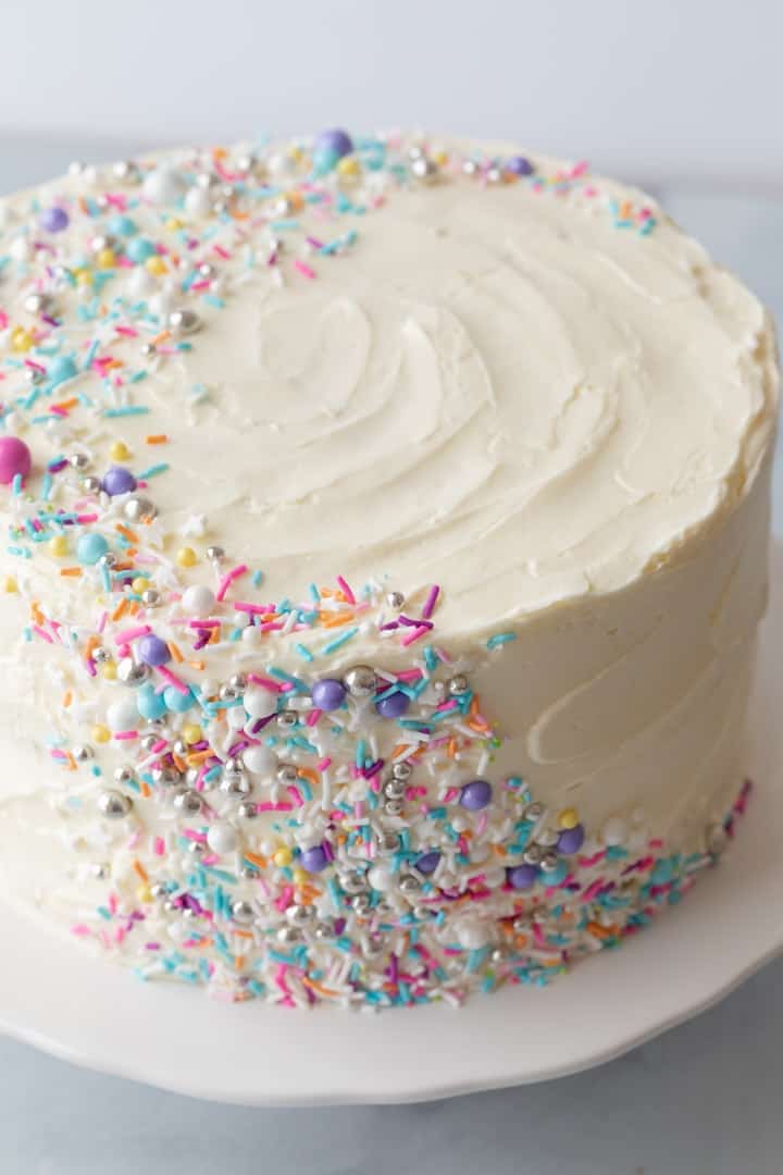 angled view of frosted funfetti cake on white cake platter