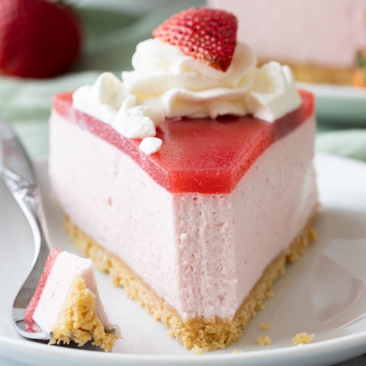 front of a slice of strawberry mousse cake with a fork taking a bite out