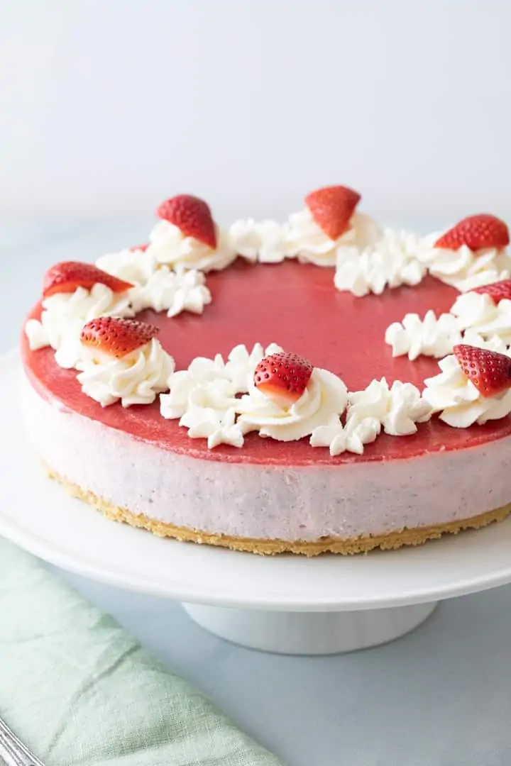 angled view of a strawberry mousse cake on a white cake stand