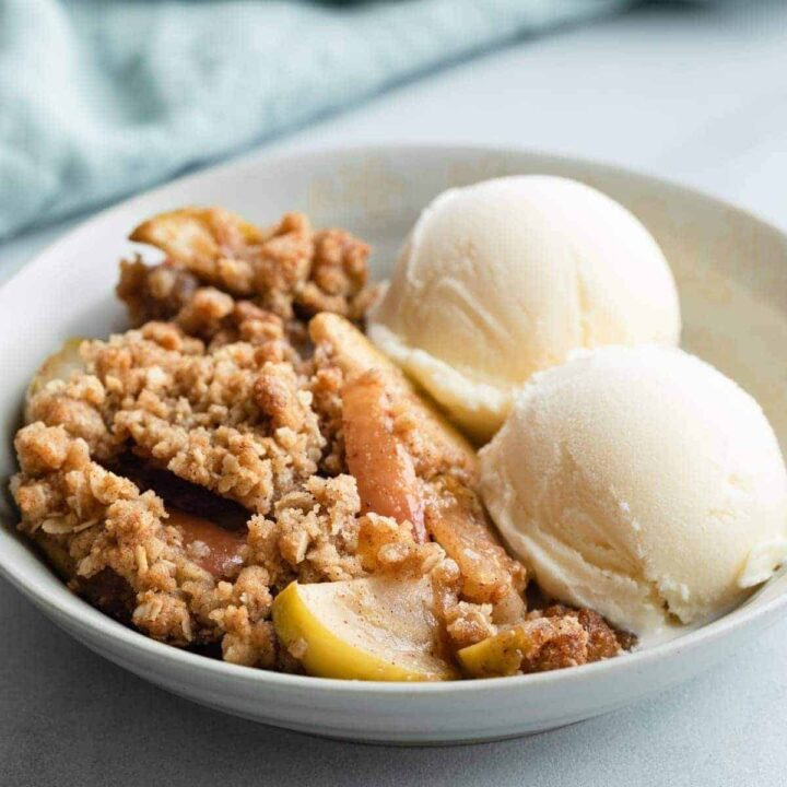 side view of apple crisp in grey bowl with 2 scoops of vanilla ice cream