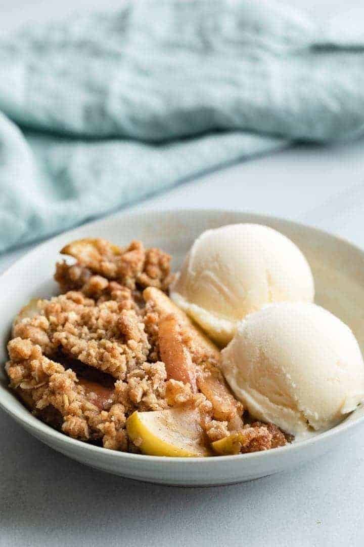side view of apple crisp in grey bowl with 2 scoops of vanilla ice cream