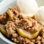 close up of apple crisp in bowl with 2 scoops of vanilla ice cream