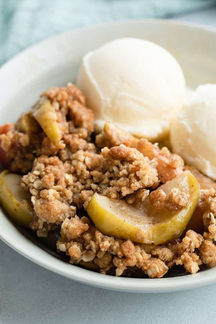 close up of apple crisp in bowl with 2 scoops of vanilla ice cream