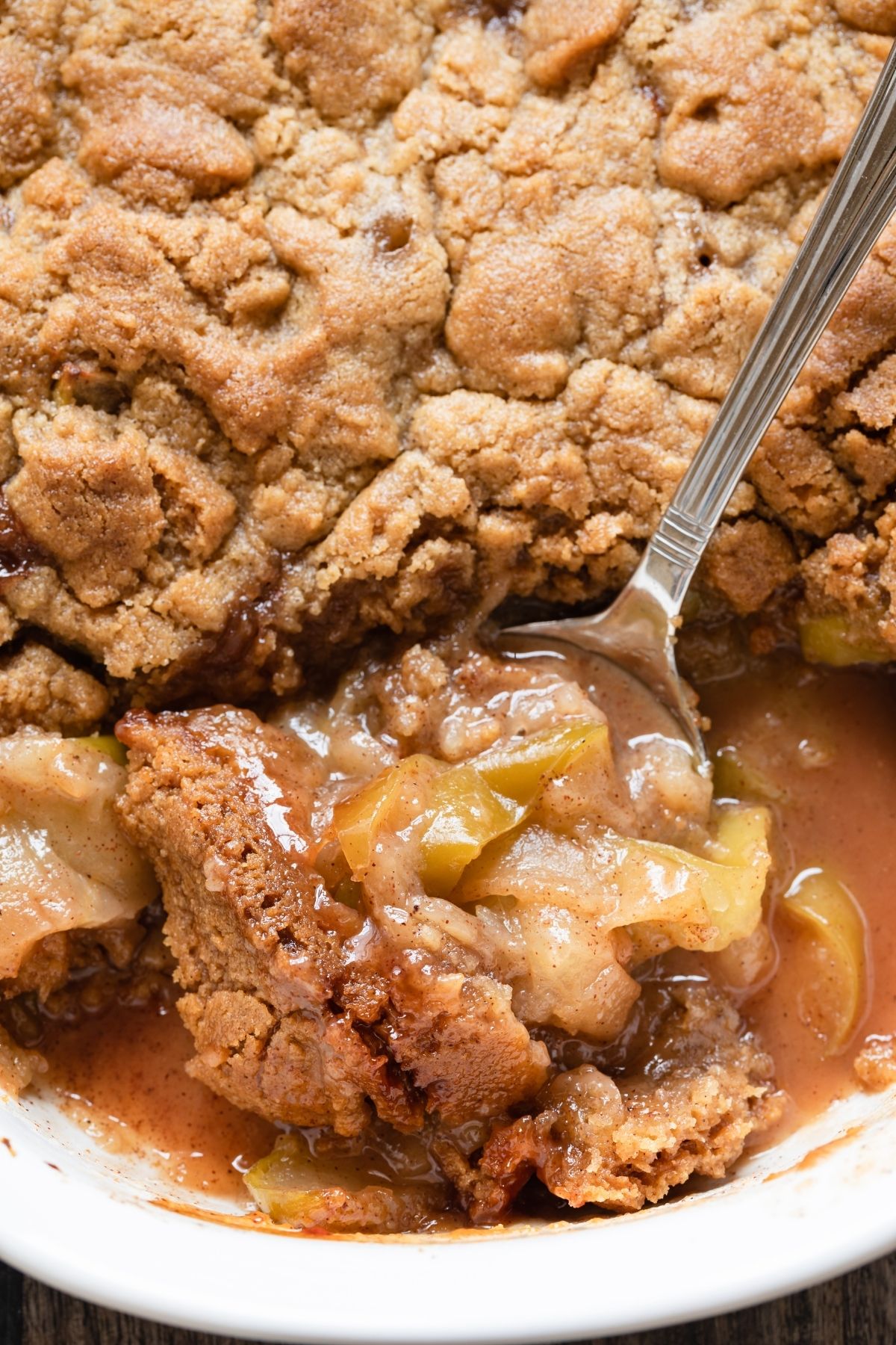 close up of apple crumble in a white baking dish with a spoon