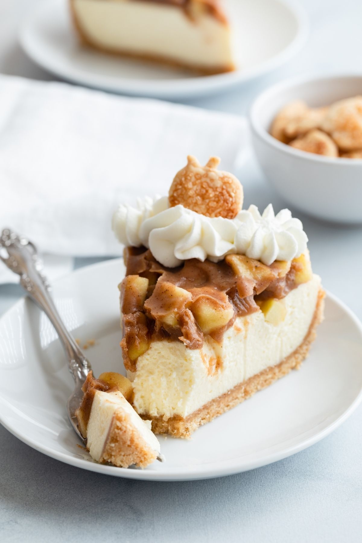 slice of apple pie cheesecake on white plate with fork taking a bite out