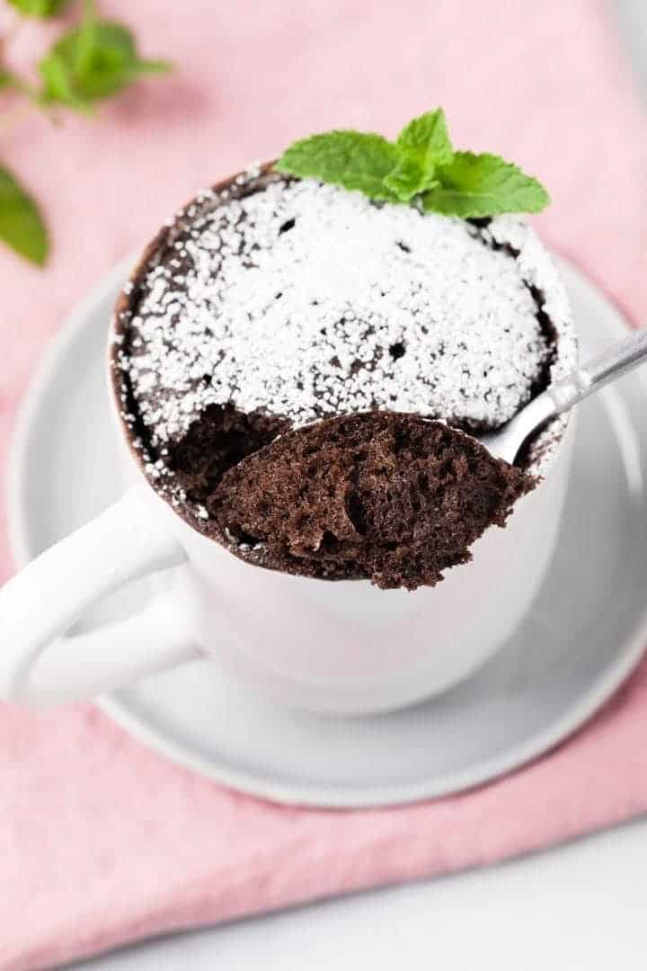 angled view of chocolate mug cake with a spoon taking a bite out