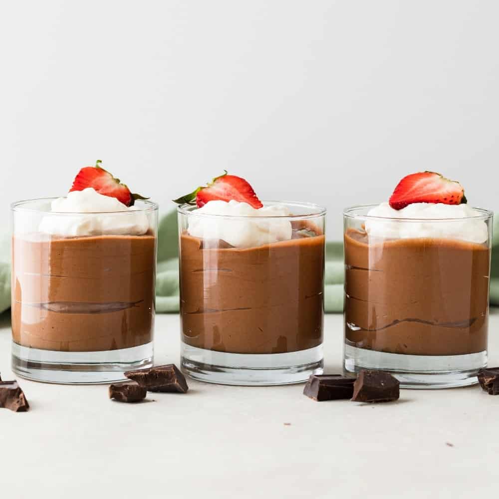 Three glasses of chocolate mousse topped with whipped cream.