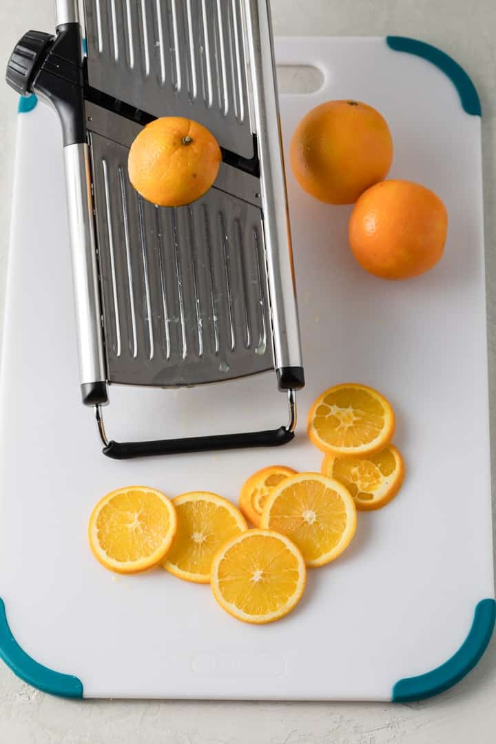 sliced oranges on a white cutting board with a mandolin