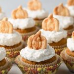pumpkin cupcakes with whipped cream and pie crust cutouts arranged neatly on a white tabletop