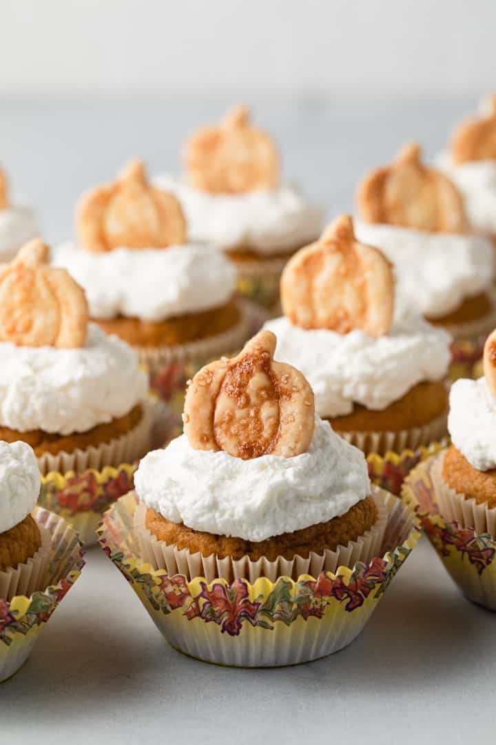 pumpkin cupcakes with whipped cream and pie crust cutouts arranged neatly on a white tabletop