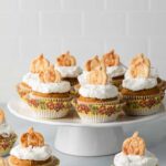 Pumpkin cupcakes with whipped cream frosting and pie crust cutouts on a white cake stand