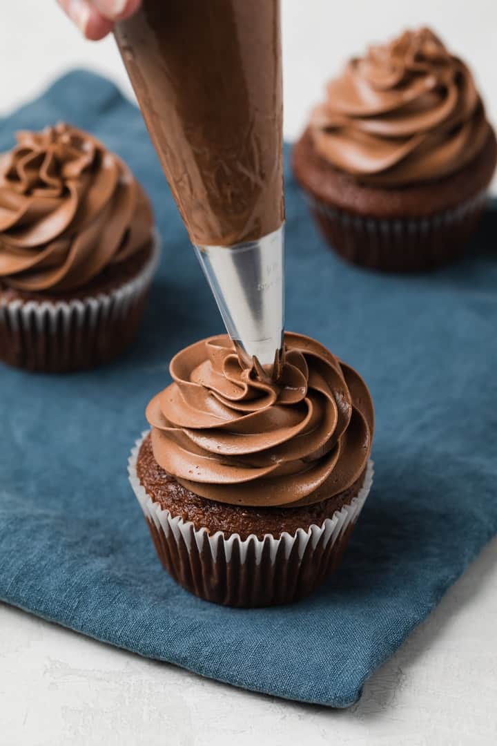 chocolate Swiss meringue buttercream being piped onto chocolate cupcakes