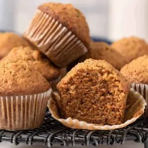 A stack of carrot muffins and one has a bite taken out.