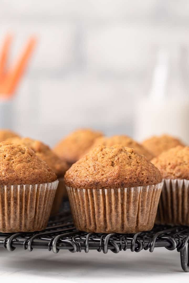 Carrot muffins in white paper liners on a black wire rack.