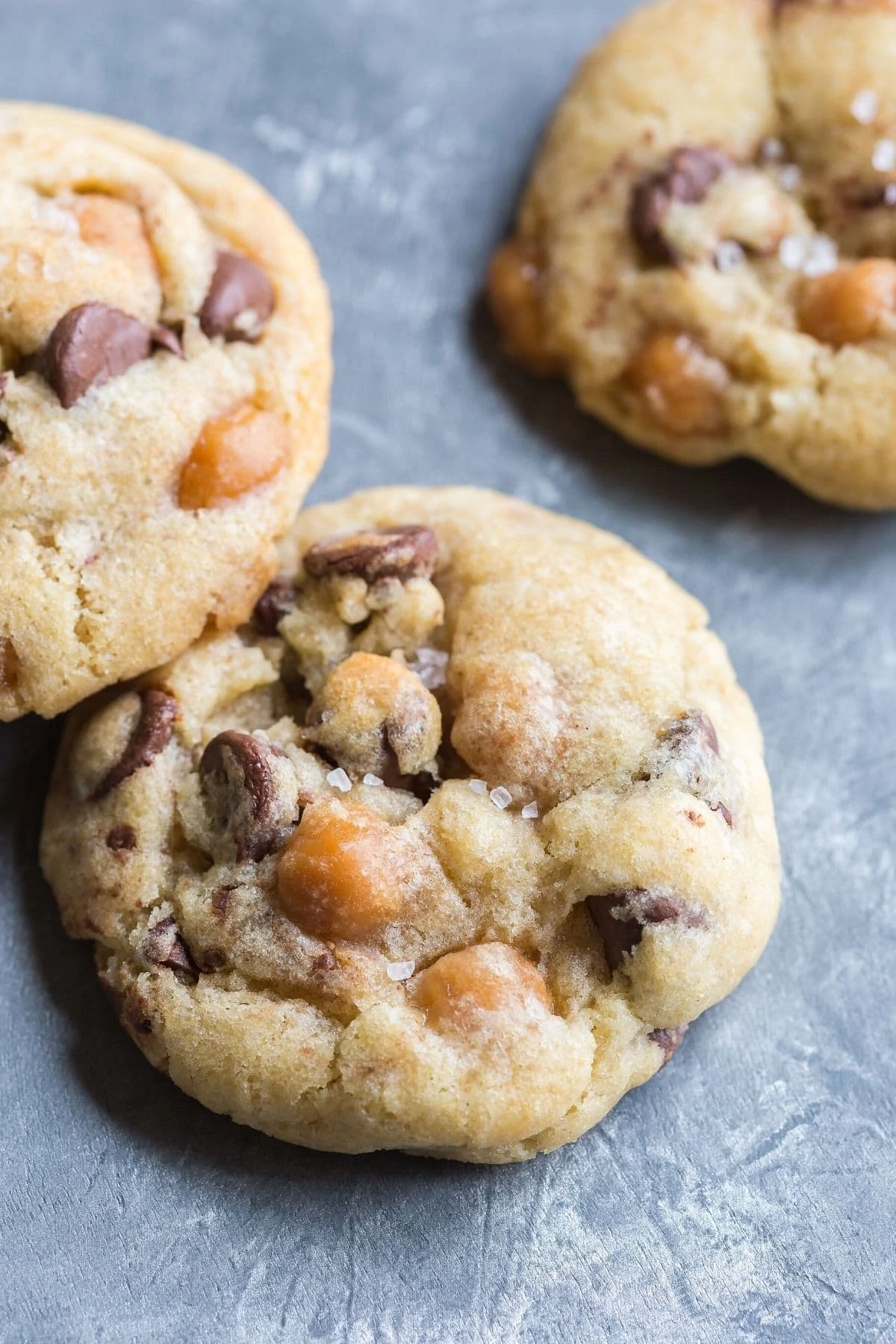 Angled view of Chocolate Chip Salted Caramel Cookies on a silvery blue background.