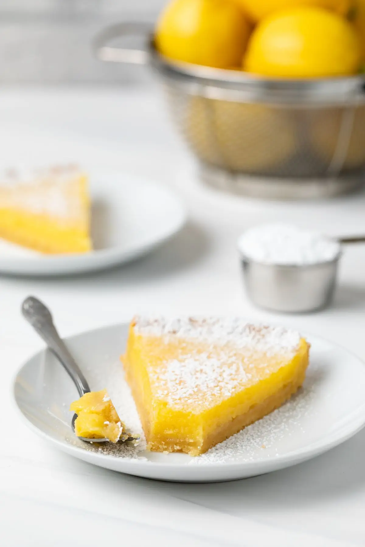 Fork taking a bite out of Tarte au Citron slice on white plate.